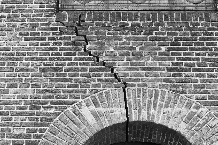 Stair-step crack running through the mortar joints of a brick wall down to an arch