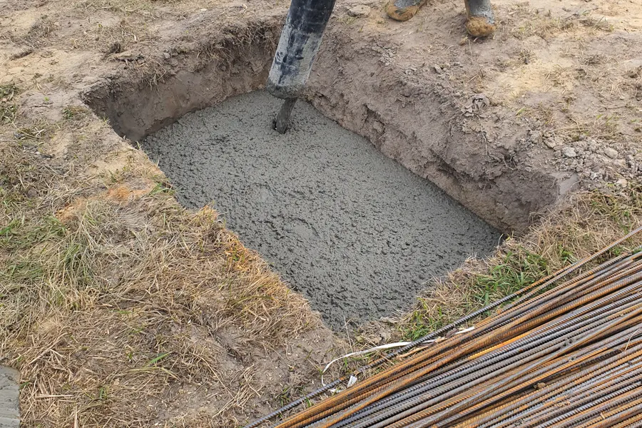 Fresh concrete poured into an excavated footing hole beside a stack of rebar