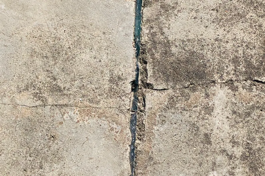 Close-up of a wide, open crack in a concrete surface with smaller cracks branching off